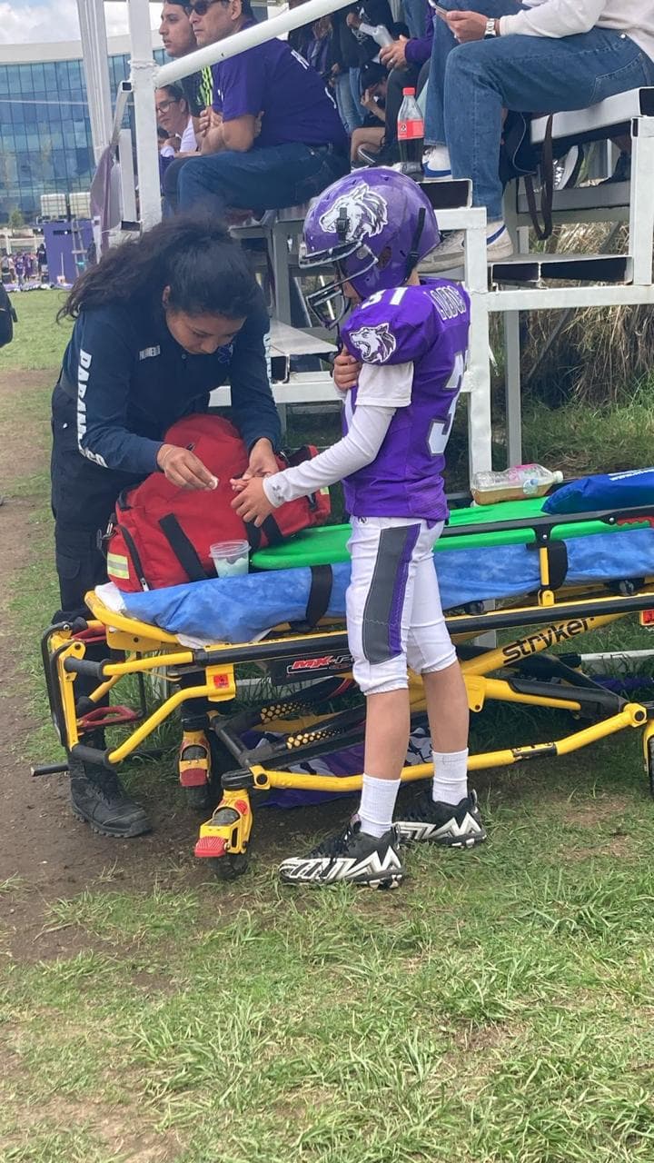 Paramédica de CASSEI atendiendo a un niño jugador de fútbol americano junto a la camilla